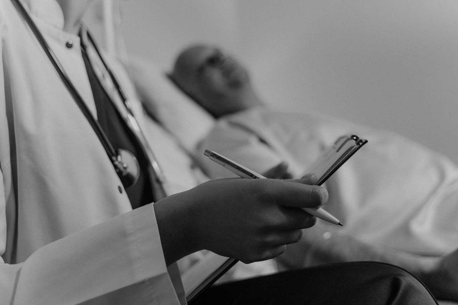 Clinician taking notes on a chart beside a patient in a hospital bed